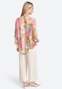 Floral blouse featuring pink, yellow, and green patterns, long sleeves, and a rounded hem; paired with cream wide-leg trousers and light shoes.