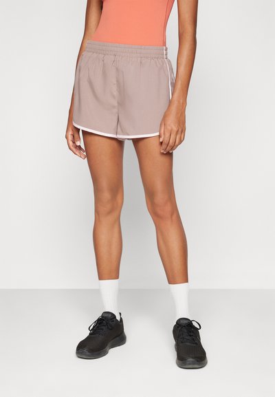 Pantaloni sportivi color beige chiaro con cintura elasticizzata, strisce bianche sui lati e una vestibilità rilassata, abbinati a sneakers nere e calze bianche.