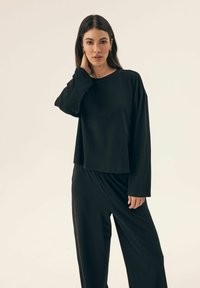 Czarna bluzka z długim rękawem o luźnym kroju i okrągłym dekolcie, zestawiona z czarnymi spodniami o szerokich nogawkach; gładki materiał o minimalistycznym wzornictwie.