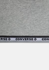 Pelēka kokvilnas krekls ar apaļu kaklu un melnu un baltu ribotu apakšmalu, kurā ir redzams "CONVERSE" emblēmas atkārtojums.