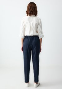 Witte lange mouwen shirt gecombineerd met marineblauwe elastische broek. De broek heeft een gladde textuur en taps toelopende pijpen, aangevuld met witte sneakers.