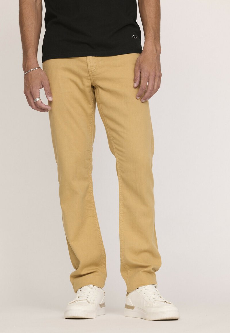 Pantalons khaki à coupe slim et jambes droites, en tissu mélange de coton. Associés à des baskets blanches et un t-shirt noir.