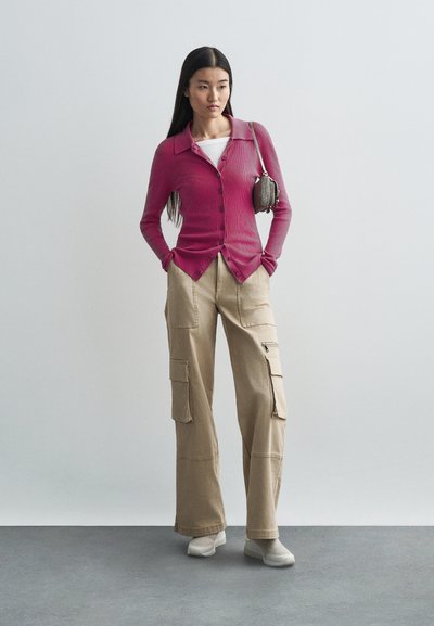 Cardigan en maille rose ajusté avec fermeture à boutons, associé à un pantalon cargo beige avec plusieurs poches et une coupe décontractée.