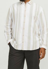 Koszula z długim rękawem w białe i beżowe pionowe paski. Luźny krój, lekki materiał i beżowe guziki.