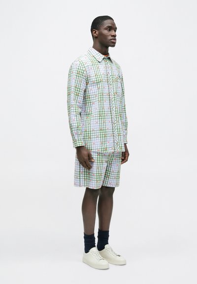 Κοντομάνικο καρό πουκάμισο και ταιριαστό σορτς με πράσινα, λευκά και κόκκινα σχέδια· κατασκευασμένα από ελαφρύ ύφασμα· συνδυασμένα με κρεμ παπούτσια και ναυτικούς κάλτσες.