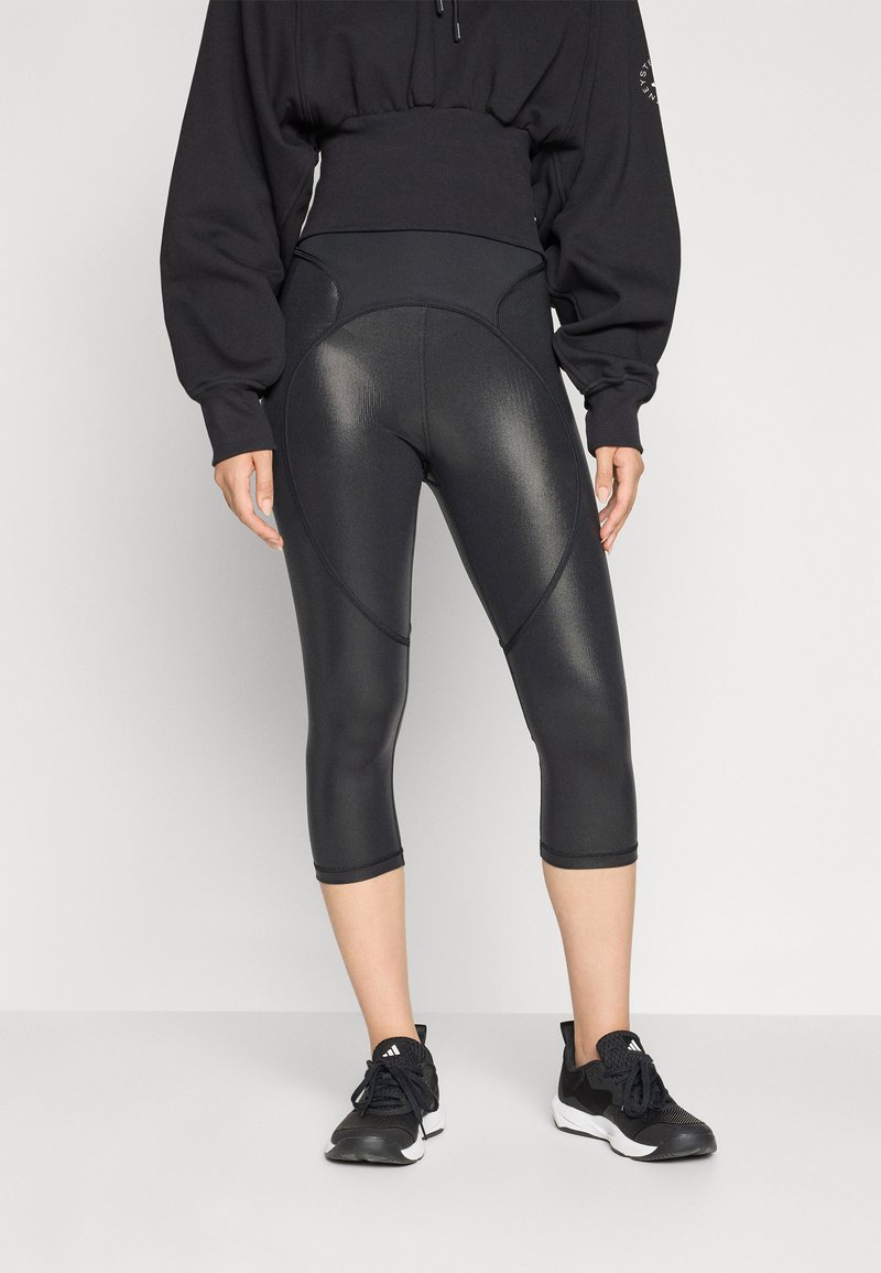 Fekete, magas derekú leggings, bordázott textúrával és térdig érő szabással, egy fekete, oversized pulóverrel és sportcipőkkel párosítva.