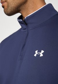 Πουλόβερ ναυτικού μπλε με ψηλό γιακά και μπροστινό φερμουάρ έως τη μέση. Διαθέτει λευκό λογότυπο στο στήθος. Κατασκευασμένο από απαλό, υφασμάτινο ύφασμα με  υφή.