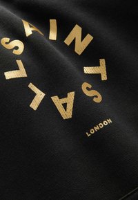 Tela negra con un texto dorado audaz dispuesto en un patrón circular, donde las palabras "SAINTS" y "LONDON" se muestran de forma destacada.