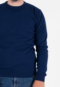 Granatowy sweter dzianinowy z okrągłym dekoltem, długimi rękawami i ściągaczami. Miękka struktura, minimalne logo na dolnej stronie.