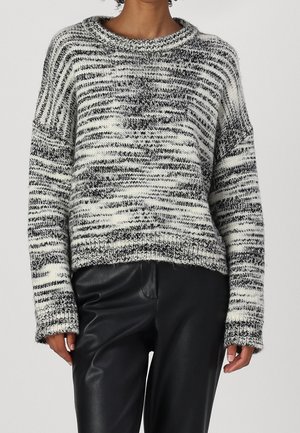 Femme portant un pull en tricot chiné noir et blanc avec un col rond, associé à un pantalon en cuir noir.