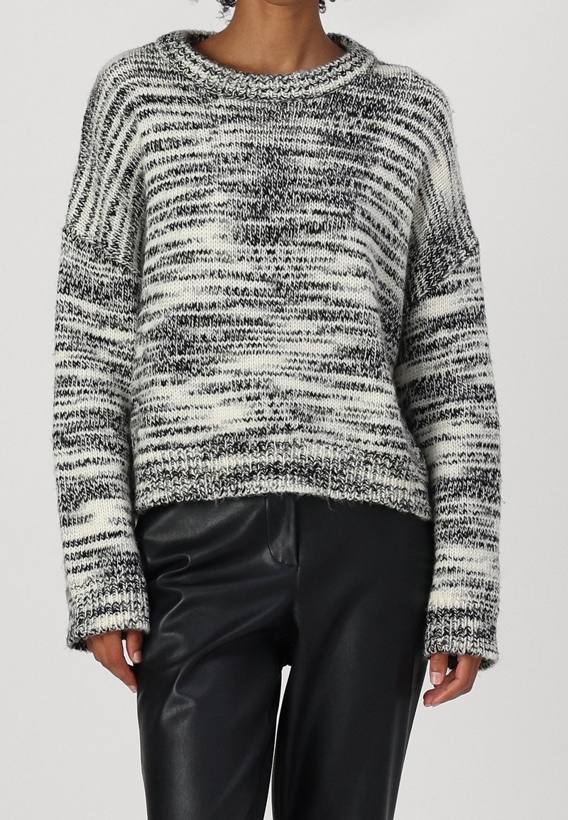 Femme portant un pull en tricot chiné noir et blanc avec un col rond, associé à un pantalon en cuir noir.