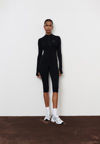 Fekete aktív viselet készlet hosszú ujjú felsővel, negyed cipzárral és magas derekú capri leggingszel. Puha, rugalmas anyag. Fehér logó részlet.