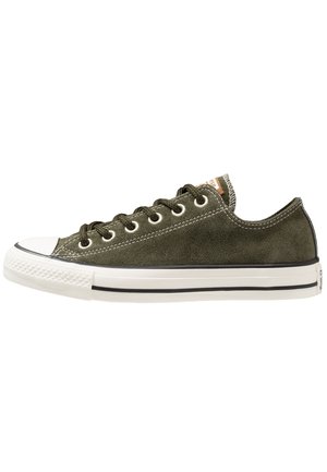 Low-top olivengrøn ruskind sneaker med hvid gummi tåhætte, sorte snørebånd og hvid sål med sort stribe.