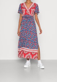 Maxiklänning med ett rödblått blommönster och paisleydetaljer, korta ärmar, knytning i midjan och en sidoklyfta, kombinerad med vita sneakers.