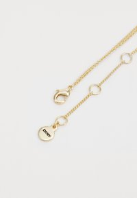 Collana in oro con chiusura a molla, anelli circolari e pendente rotondo inciso con "DKNY". Texture metallica liscia.