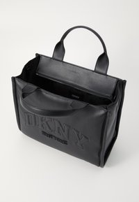 Melna ādas rokassoma ar iegravētu "DKNY" logo, divi izturīgi rokturi, ārējais rāvējslēdzēja kabata, gluda virsma un atvērta iekšpuse.