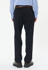 Černé kalhoty z texturované tkaniny, rovného střihu, se dvěma zadními kapsami, v kombinaci s hnědými koženými botami a hnědým opaskem.