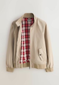 Bézs dzseki cipzáras elülső résszel, bordázott mandzsettákkal és zsebbel. Bélése piros-fehér kockás szövet kontrasztként. Álló gallér kialakítással.