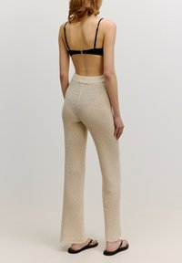 Beige, gebreide, wijde broek met een textuurpatroon, gecombineerd met een zwarte, rugloze top en zwarte sandalen. De tailleband is elastisch.