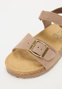 Tan mockasinsandaler med en bred rem och en justerbar spänne i guldton. Korksål med en texturerad yta. Lätta och öppna i designen.