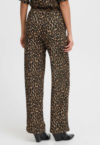 Pantalons larges en imprimé léopard en tissu doux, avec une taille haute et une texture lisse ; associés à des chaussures à talons noires.
