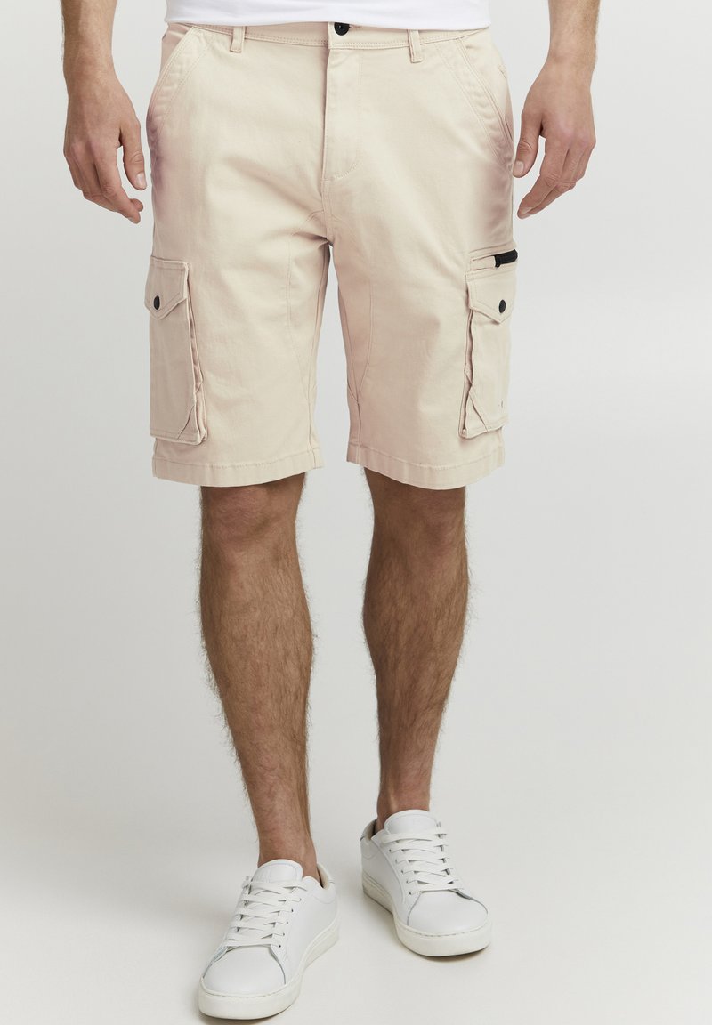 Shorts cargo beiges en coton avec deux poches latérales et une poche zippée. Présente un design à jambe droite et un ourlet cousu.
