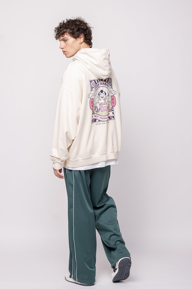 Sudadera oversize color crema con un estampado gráfico en la parte de atrás. Combinada con pantalones de chándal verde oscuro con rayas blancas en los laterales.