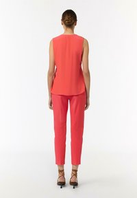 Korale bezrękawnik i dopasowane spodnie, wykonane z gładkiego materiału. Uzupełnione o brązowe sandały na wysokim obcasie, widok z tyłu.