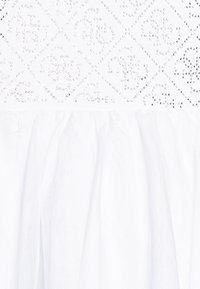 Tissu blanc avec un motif en diamant agrémenté de petites embellissements brillants. Le bas présente une texture froncée et transparente.