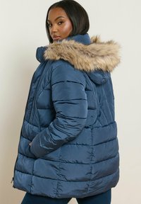 Mörkblå puffjacka med en foderhuva av päls, med quiltade sektioner, framfickor och blixtlåsstängning. Mjuk, glänsande textur.