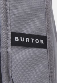 Gray fabric with a textured weave, featuring a black label with white lettering that reads "BURTON." Clean design with visible stitching details.