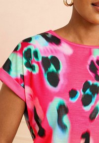 Krátky rukáv top v žiarivej ružovej farbe s abstraktným čiernym a tyrkysovým leopardím vzorom, s okrúhlym výstrihom a jemnou, ľahkou tkaninou.