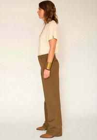 Haut beige à manches courtes associé à un pantalon large taille haute marron. Les accessoires comprennent des bracelets en or et des chaussures plates marron.
