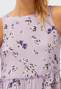 Lichtpaarse mouwloze jurk met bloemenpatroon. Bevat kleine witte en paarse bloemen, een gerimpelde zoom en een gladde textuur.