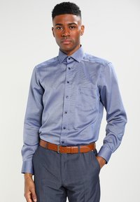 Long-sleeve blue button-up shirt with subtle texture, collar, and chest pocket; paired with gray trousers and a brown belt.