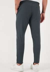 Donkergrijze sportbroek met een taps toelopende pasvorm, elastische tailleband, zijzakken en een gladde, lichtgewicht stof; gedragen met witte sneakers.