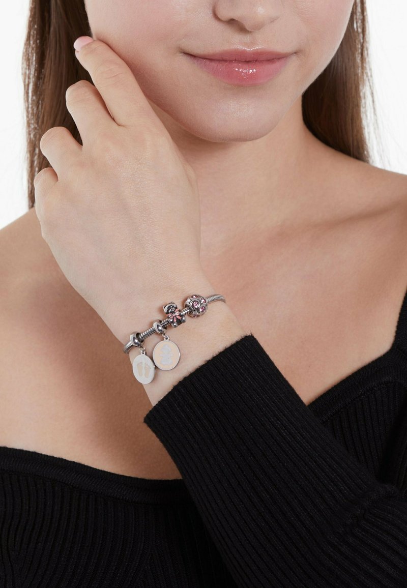 Silbernes Charm-Armband mit pinken Akzenten, dekorativen Perlen und zwei Anhängern, die Design von Fuß und Baby zeigen. Am Handgelenk getragen.