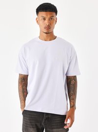 Camiseta de algodón de manga corta en lavanda claro con cuello redondo. Presenta un sutil diseño bordado en el pecho. Combinada con vaqueros oscuros.