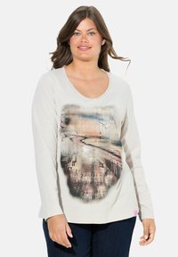 Helles beige Langarmshirt mit rundem Ausschnitt. Verfügt über ein bedrucktes Küstenszenario in sanften Pastellfarben. Strukturierter Stoff mit einem Etikett am Saum.