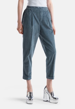 Pantaloni in corduroy azzurro chiaro con pieghe, gambe affusolate e risvolti. Indossati con scarpe con tacco alto metallico per creare un contrasto.