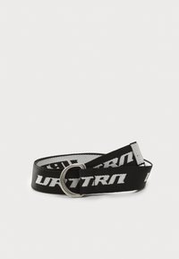 Zwarte riem van geweven stof, met een grote metalen ringgesp en witte "ULTRA"-tekst die in een herhaald patroon is bedrukt.