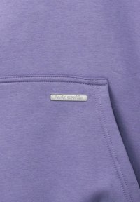 Lila Sweatshirtstoff mit einer glatten Textur, versehen mit einem kleinen metallischen Etikett mit "basic republic" auf der Vordertasche.