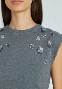 Top sin mangas en gris que presenta adornos florales texturizados en varios tonos de gris y acentos metálicos en la parte frontal.