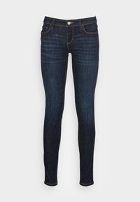 Jeans ajustados de mezclilla azul oscuro con una silueta ajustada, diseño de cinco bolsillos, cierre de botón y costuras con detalles en hilo amarillo.