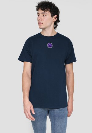 Navy cotton t-shirt with short sleeves and a round neckline. Features a purple circular embroidered emblem at the chest.