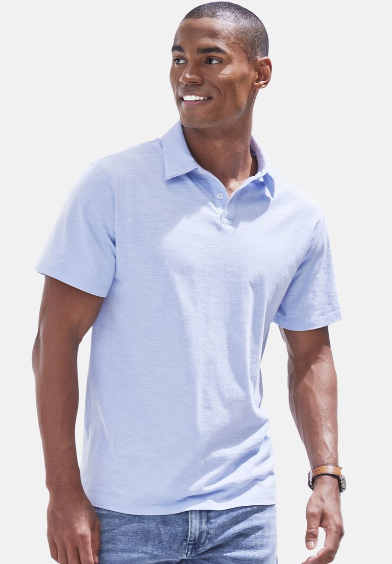 Polo de manga corta azul claro con cuello, que presenta una textura sutil y una tapeta de tres botones, combinado con jeans de mezclilla.
