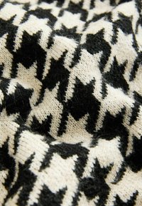 Pleteno platno s uzorkom houndstooth u crnoj i krem boji, prikazujući teksturiranu površinu s vidljivim vlaknima.