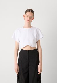 Λευκή κοντομάνικη μπλούζα κομμέ�νη με στρογγυλή άκρη, φτιαγμένη από απαλό ύφασμα. Συνδυασμένη με μαύρο παντελόνι ψηλής μέσης με τσέπες.