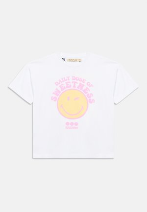 Hvit T-skjorte med korte ermer, med et stort gult blinkende smilefjes og rosa tekst "Daily dose of sweetness" på forsiden.