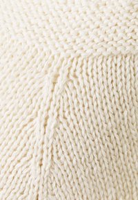 Tela de punto color crema con un patrón texturizado, que muestra puntadas retorcidas y una apariencia suave y gruesa.